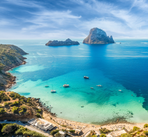 Türkisfarbene Bucht mit Es Vedrà bei Ibiza, umgeben von Booten und Felsküste.