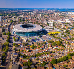 Luftaufnahme eines großen Stadions inmitten Londons, umgeben von dicht bebauten Wohnvierteln und grünen Parks.