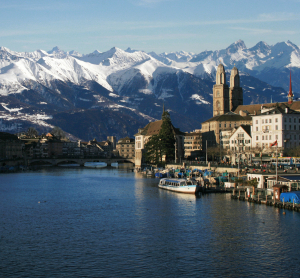 Züricher Altstadt an der Limmat mit den Kirchtürmen und schneebedeckten Alpen im Hintergrund.