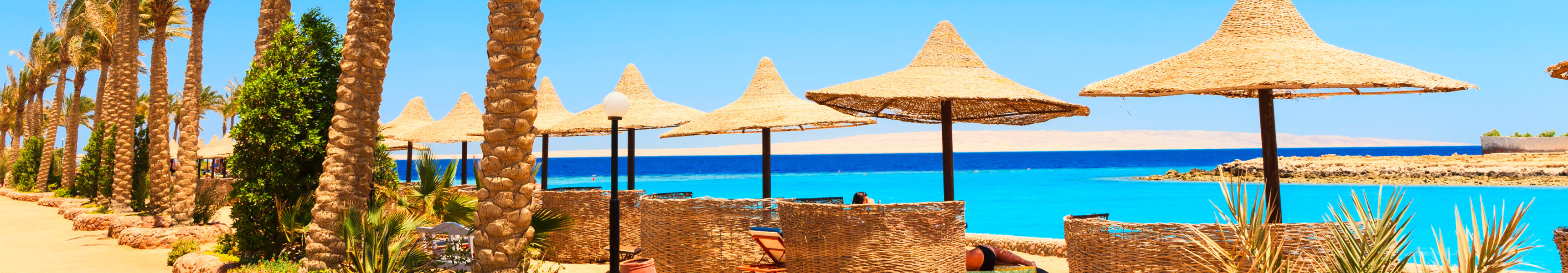 Sonniger Strand in El Gouna mit Palmen, Strohschirmen und Blick auf das Rote Meer in Ägypten
