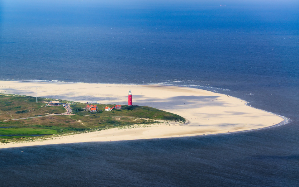 Luftaufnahme der niederländischen Insel Texel mit Sandstränden, einem roten Leuchtturm und angrenzenden Dünenlandschaften inmitten der Nordsee.