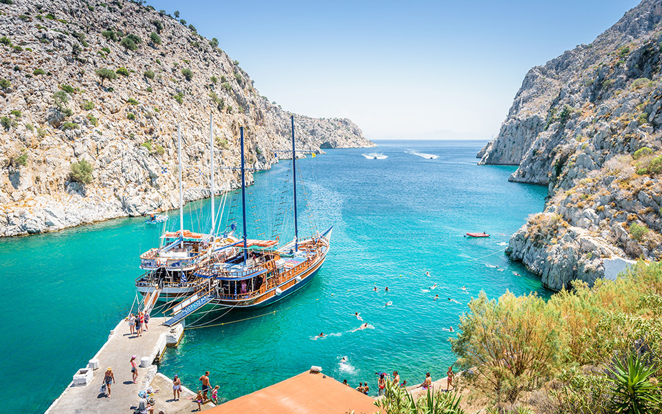 Traumhafte Bucht auf der griechischen Insel Korfu mit türkisblauem Wasser, steilen Felsklippen und einem traditionellen Segelboot