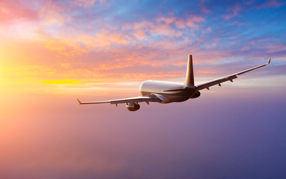 Ein Passagierflugzeug fliegt in den Sonnenuntergang, was eine typische Herausforderung für den Jetlag bei Reisen von West nach Ost darstellt.