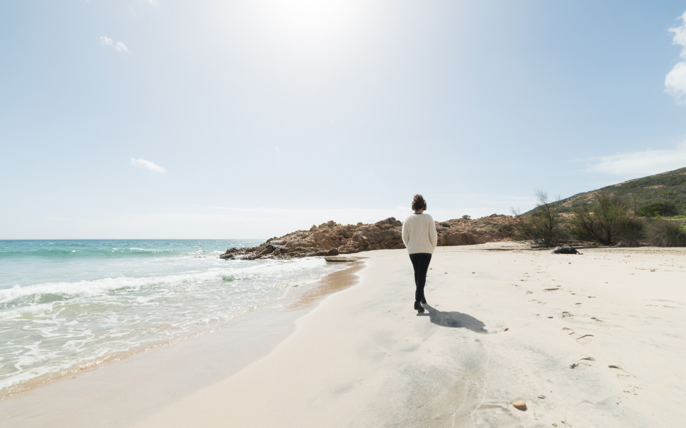 Eine Person spaziert am ruhigen Sandstrand entlang, während die Sonne scheint – eine Methode zur Anpassung des Tagesablaufs zur Vermeidung von Jetlag.