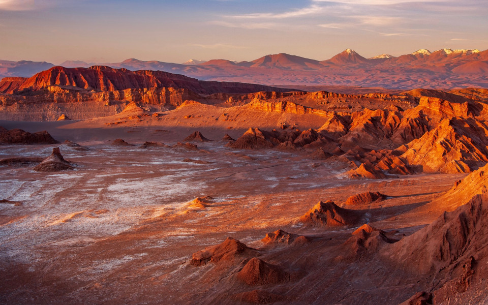 Trockene Felslandschaft im Valle de la Luna mit rötlichen Gesteinsformationen und schneebedeckten Andengipfeln im Hintergrund.