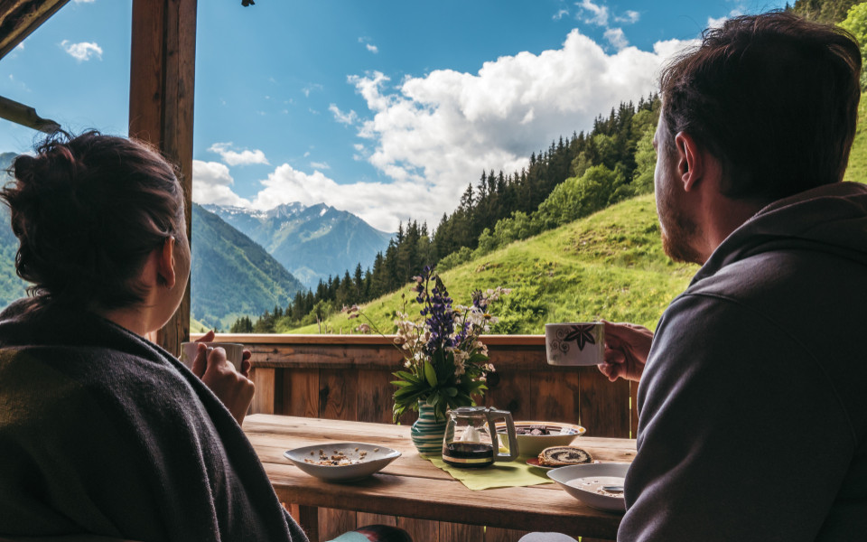 Zwei Personen sitzen auf einer Terrasse, genießen Kaffee und Gebäck, während sie auf die Berge des Berchtesgadener Landes blicken.